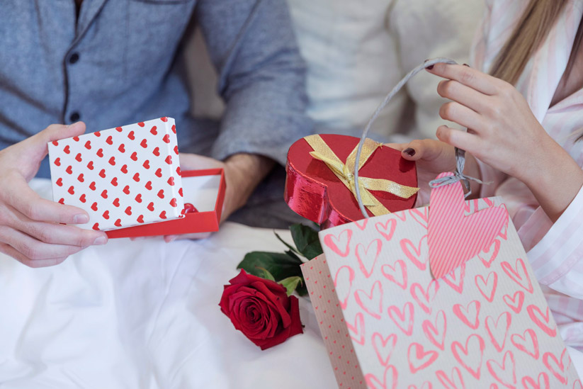 couple-pajamas-sitting-bed-with-gifts-scaled